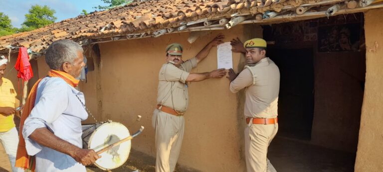 फरार आरोपी के घर पर मुनादी कर पुलिस ने किया नोटिस चस्पा।